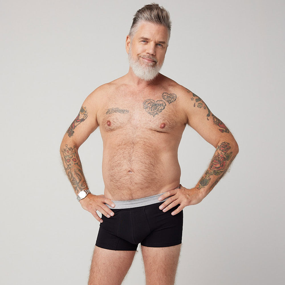 Homme tatoué portant le boxer absorbant lavable homme TENA, conçu pour l'incontinence légère, offrant protection discrète et confort.