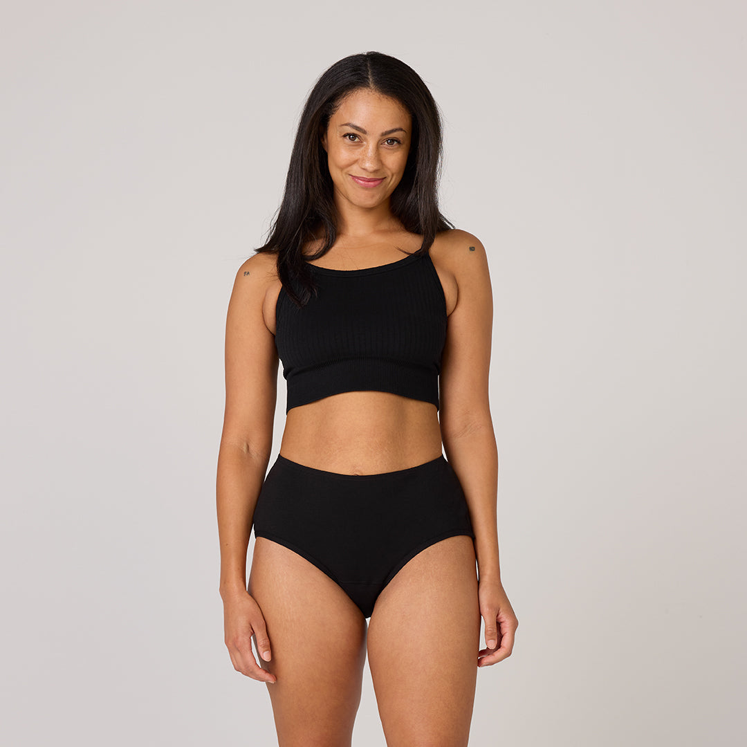 Femme portant les sous-vêtements en coton biologique TENA, montrant un débardeur noir court et une culotte taille haute, illustrant confort et style pour incontinence légère.