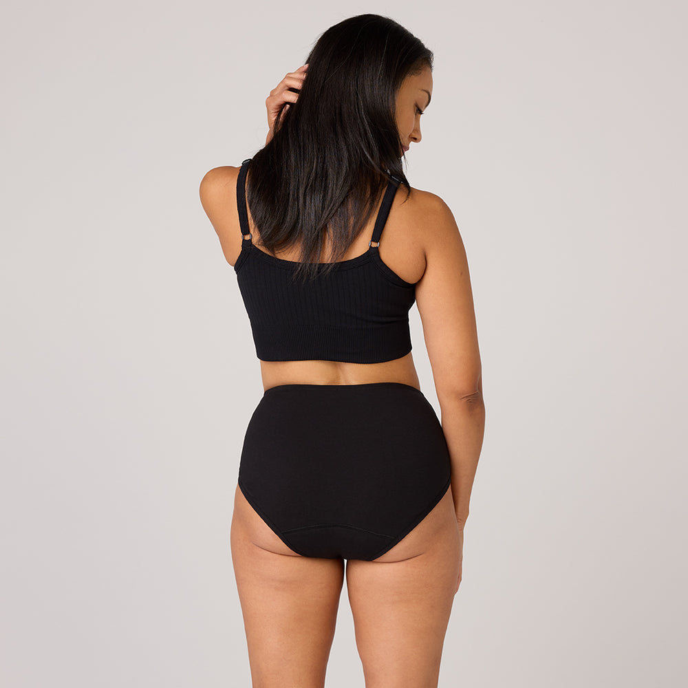 Lot de 3 sous-vêtements en coton biologique TENA, une femme porte un haut court noir et des sous-vêtements taille haute, illustrant discrétion et confort.