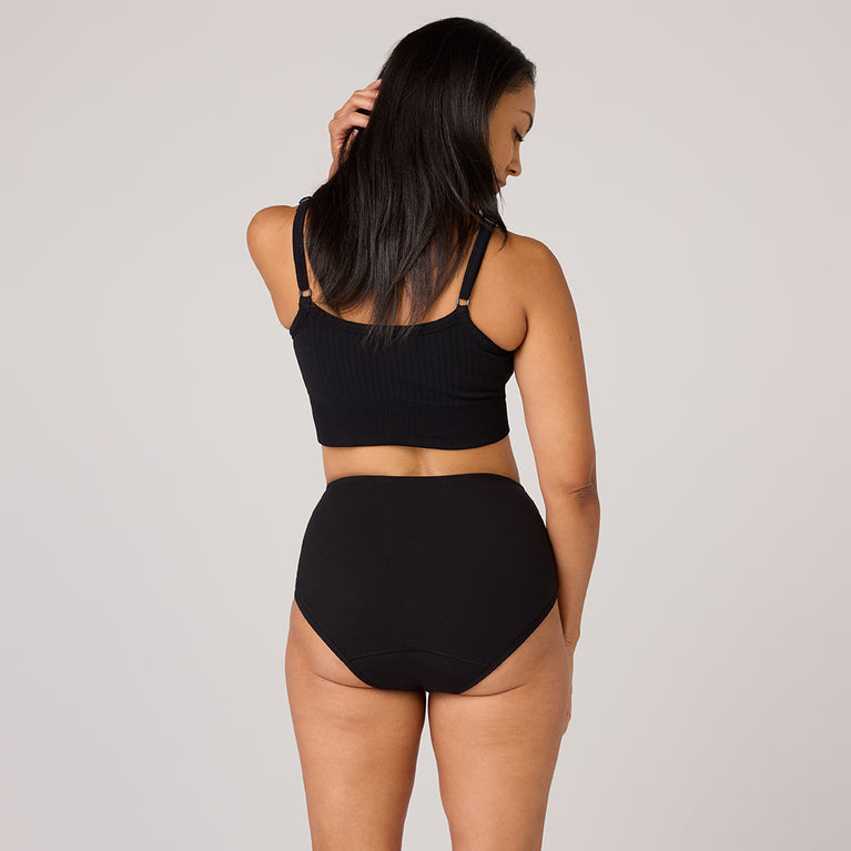 Lot de 3 sous-vêtements en coton biologique TENA, une femme porte un haut court noir et des sous-vêtements taille haute, illustrant discrétion et confort.