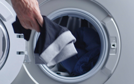 Une main d'homme met un boxer noir lavable pour hommes dans une machine à laver.