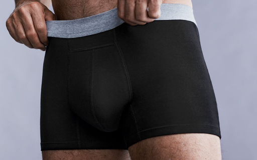 Mains d'homme ajustant un boxer noir lavable pour hommes avec une ceinture grise devant un fond gris.