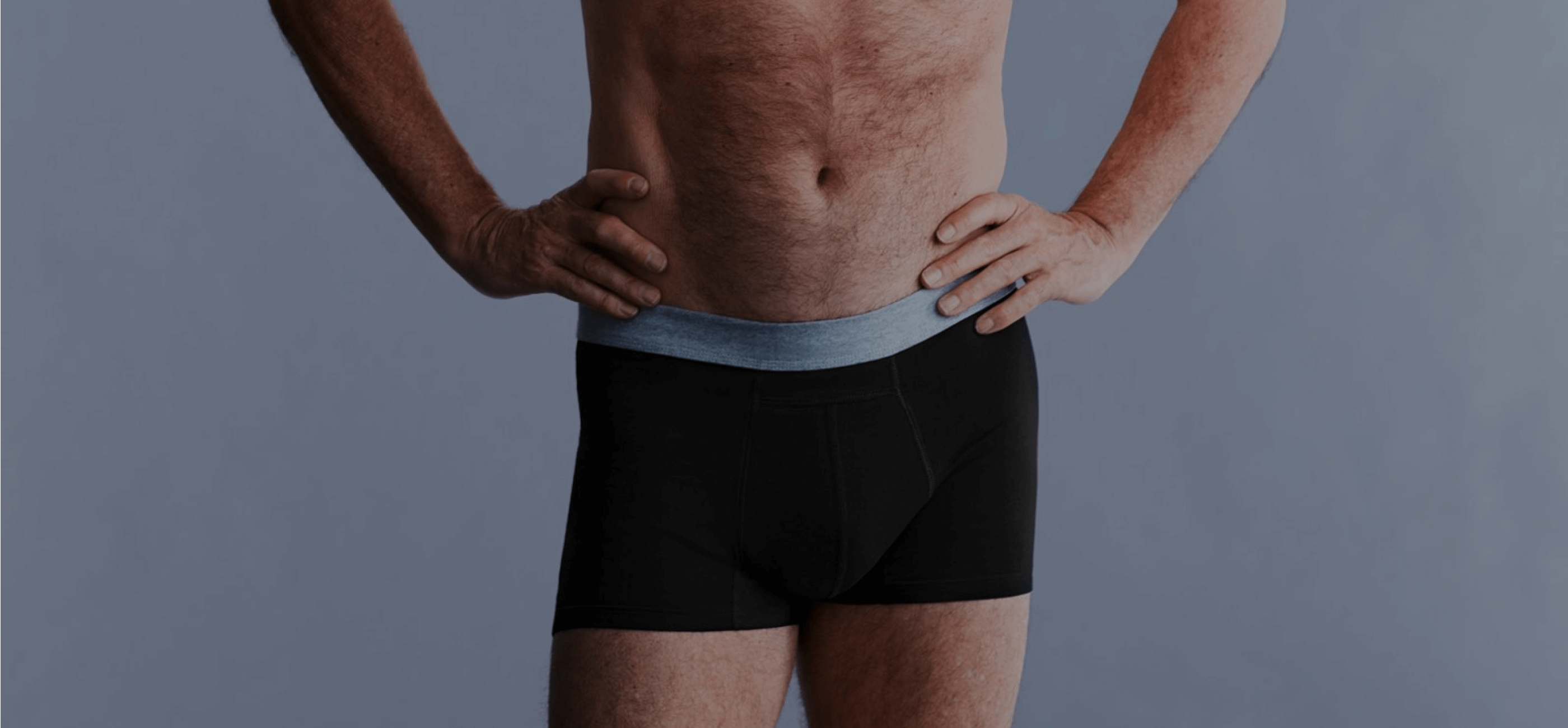 Homme torse nu portant un boxer noir lavable pour incontinence avec la main sur les hanches.